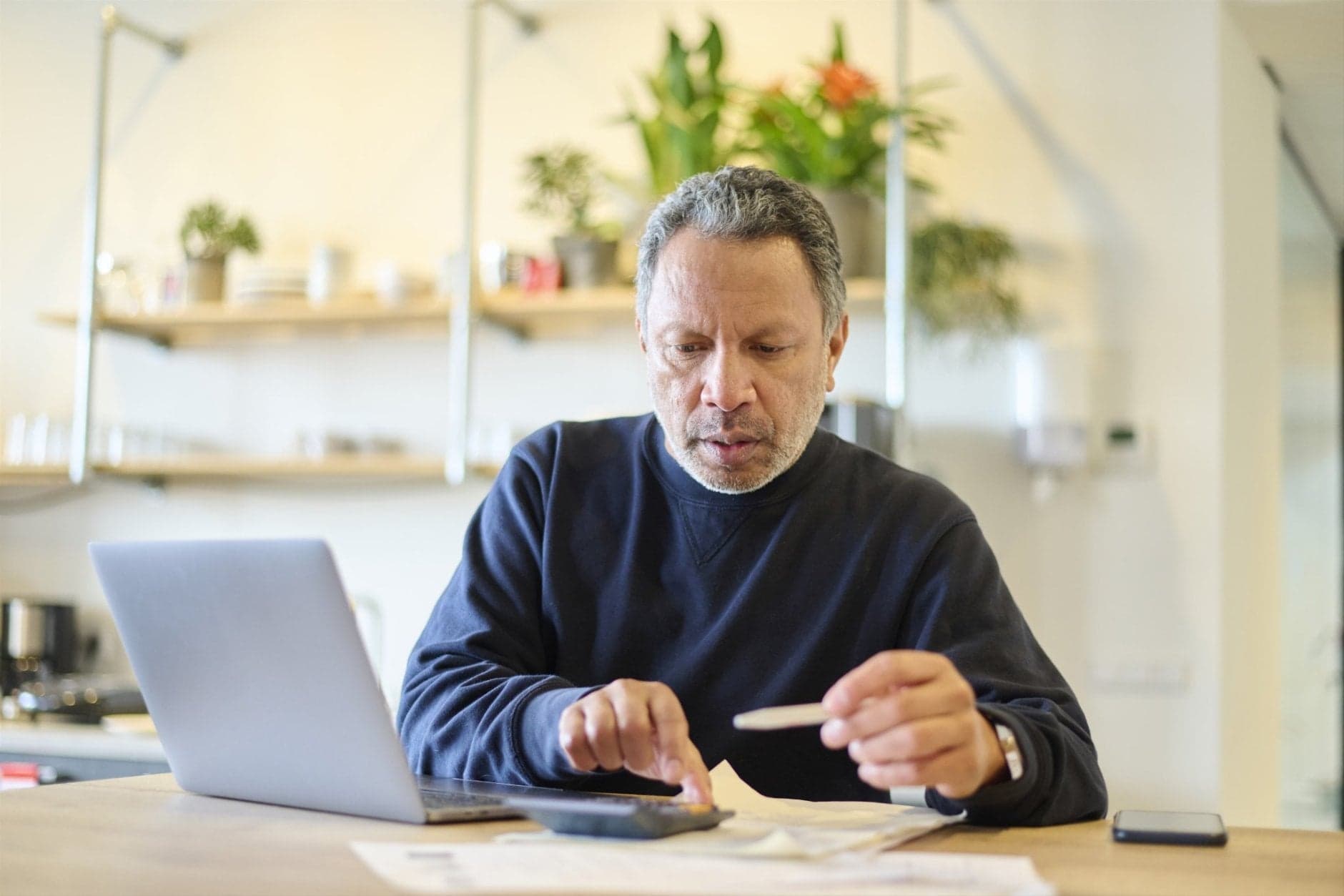 Man achter laptop met rekenmachine en papieren
