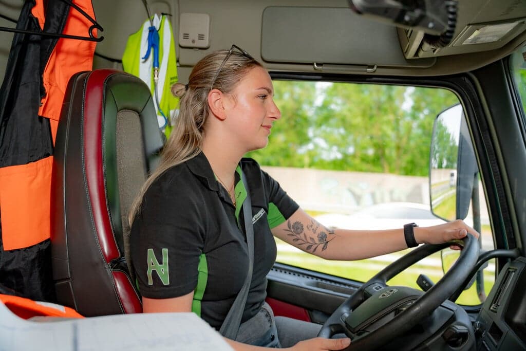 Esther Dussink achter het stuur van een vrachtwagen met achter haar veiligheidskleding