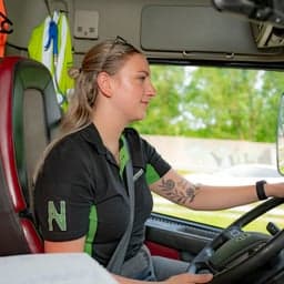 Esther Dussink achter het stuur van een vrachtwagen met achter haar veiligheidskleding