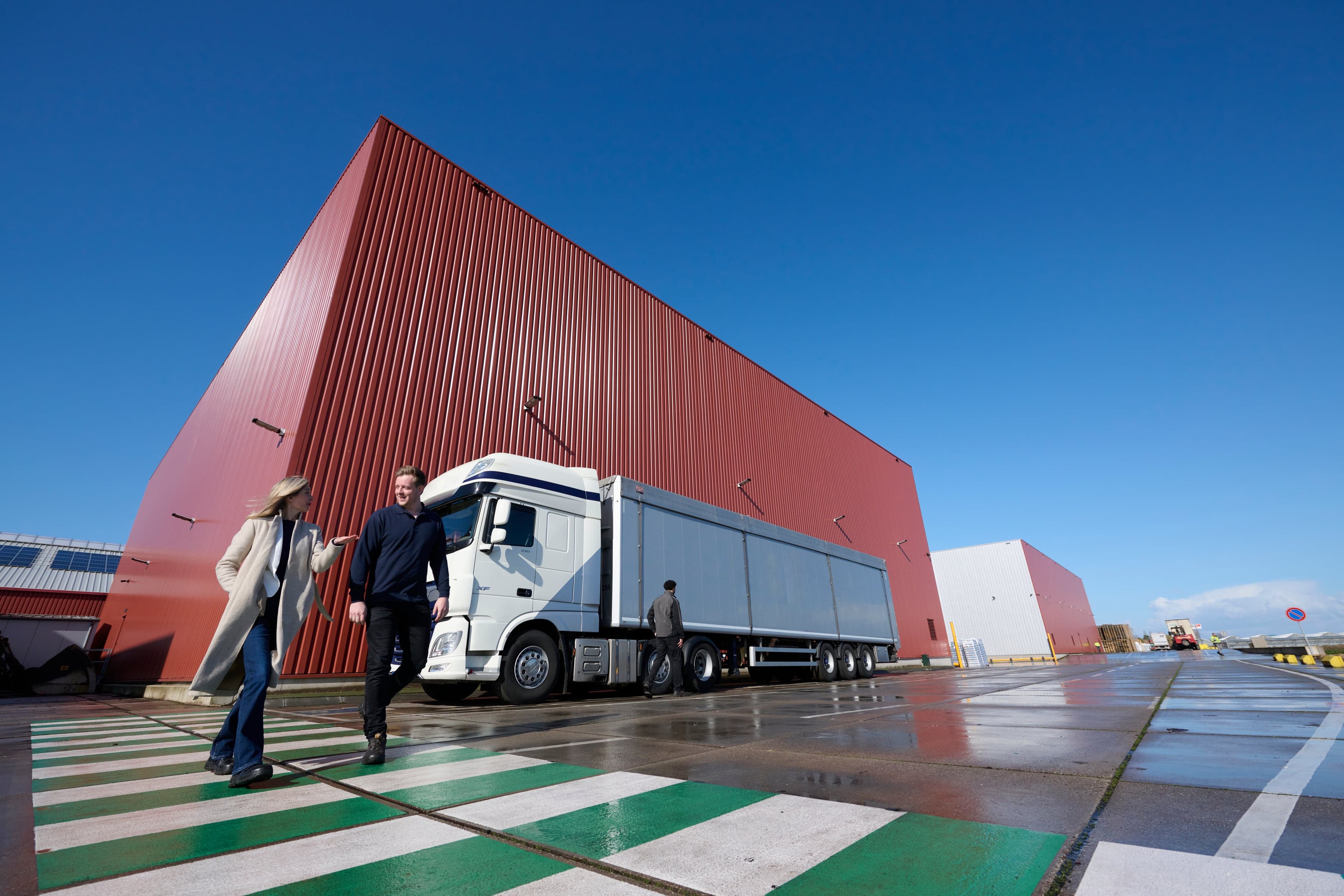 Twee mensen die overleggen en wandelen over een groen wit zebrapad voor een warehouse met vrachtwagen
