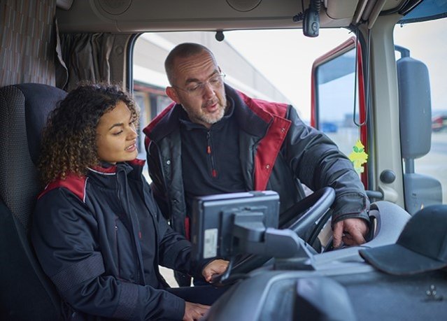 Man wijst naar dashboard in vrachtwagen, uitleg aan student-werknemer